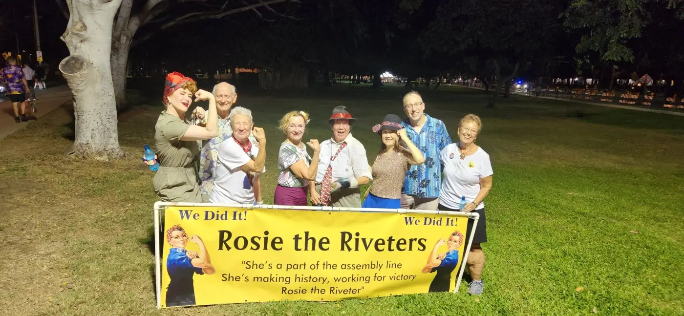 Rosie the Riveters group with banner on a lawn at night